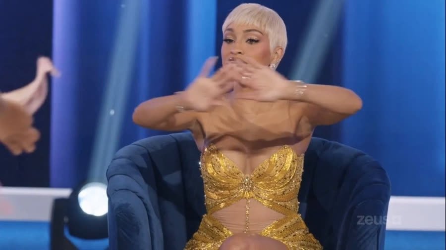 The host gesturing for calm after the altercation, seated in the reunion chair